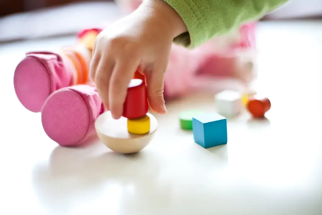 Die Hände eines Kindes ordnen geschickt bunte Holzklötze auf einem Tisch an und zeigen so Kreativität und Spielfreude.