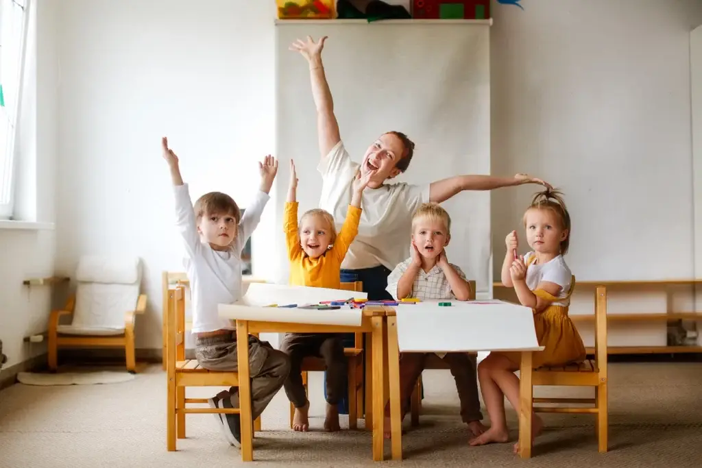 Eine Frau und Kinder an einem Tisch, die alle ihre Hände in einer Geste der Aufregung oder der Teilnahme heben.